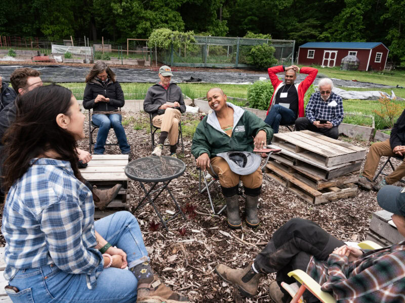 A group of people sit in a circle outside at a farm.