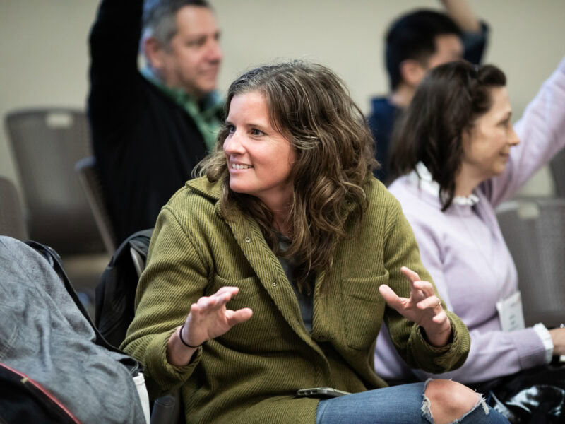 A woman sits in a boardroom, she's looking over her shoulder and smiling at someone behind her.